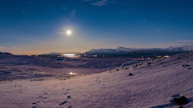 A snowy mountain landscape at night with a bright moon and distant lights.
