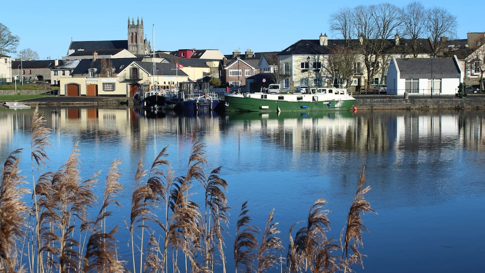 Une rivière paisible où l’on peut apercevoir des bateaux, une église et des maisons le long des rives.