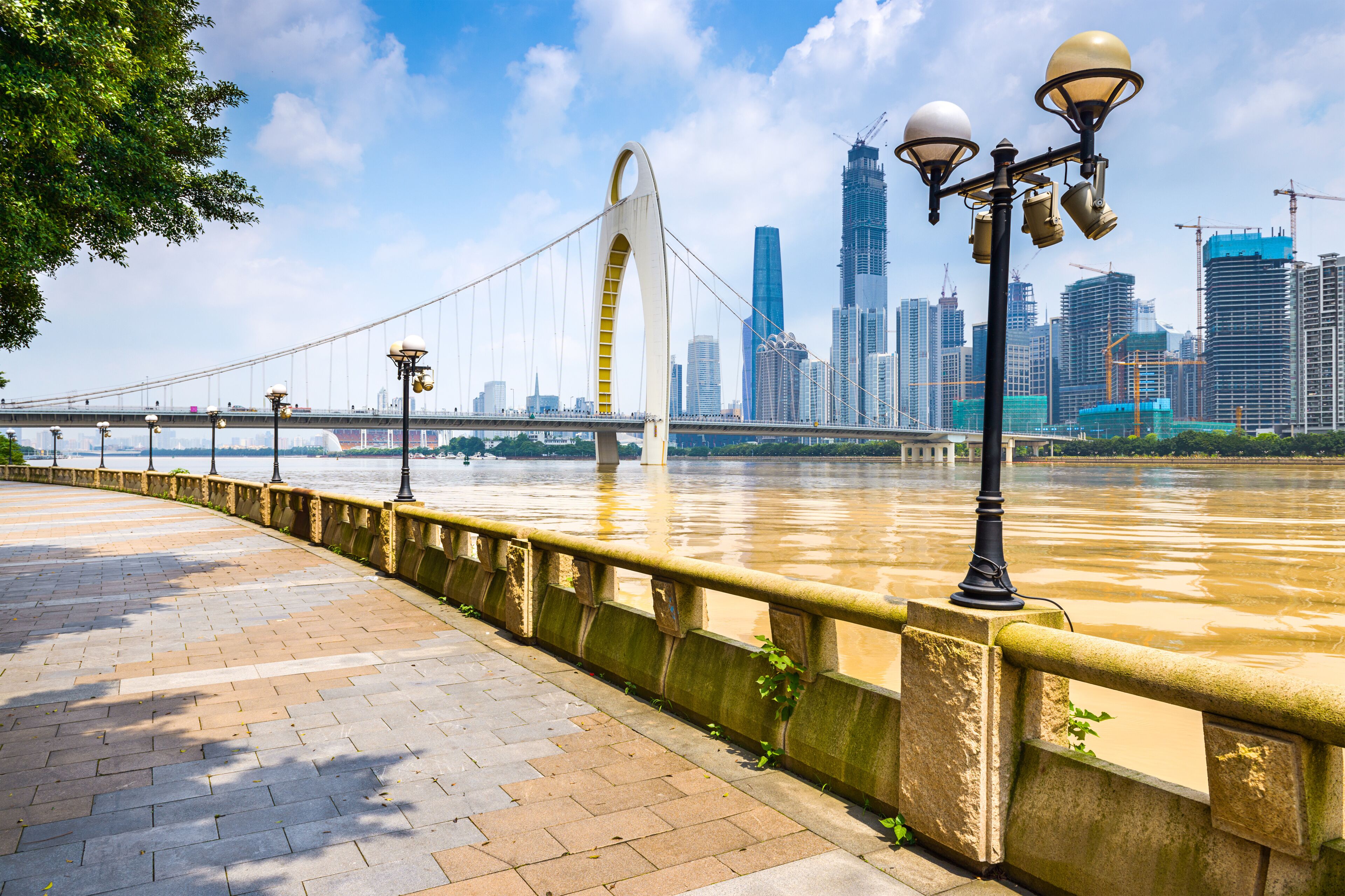 Un paseo fluvial con un puente, el perfil urbano de la ciudad y grúas de construcción.
