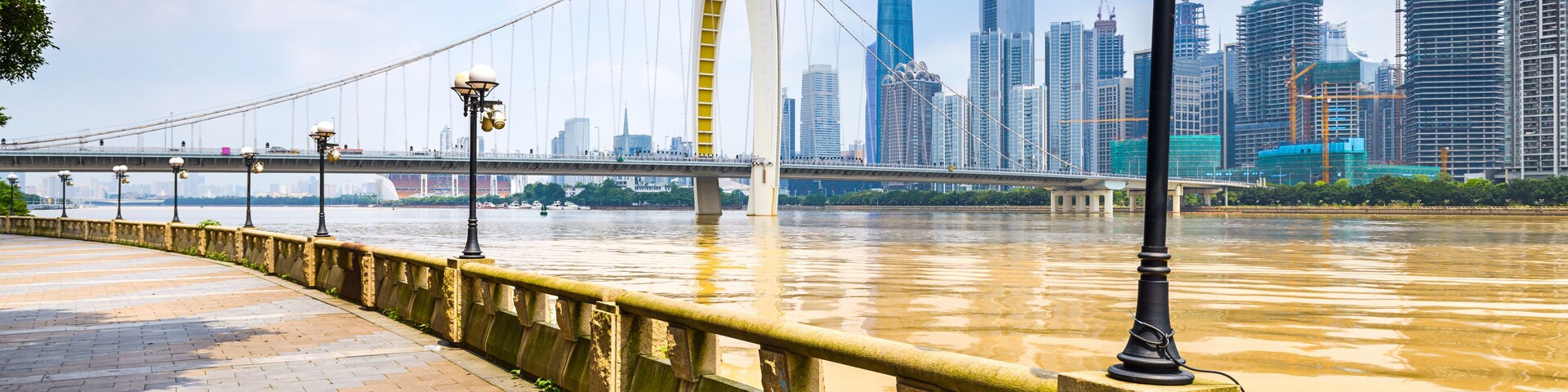Un paseo fluvial con un puente, el perfil urbano de la ciudad y grúas de construcción.