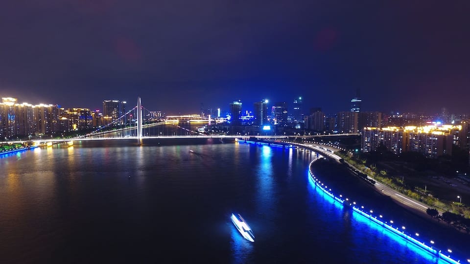 A nighttime cityscape with a prominent bridge and illuminated buildings along a river.