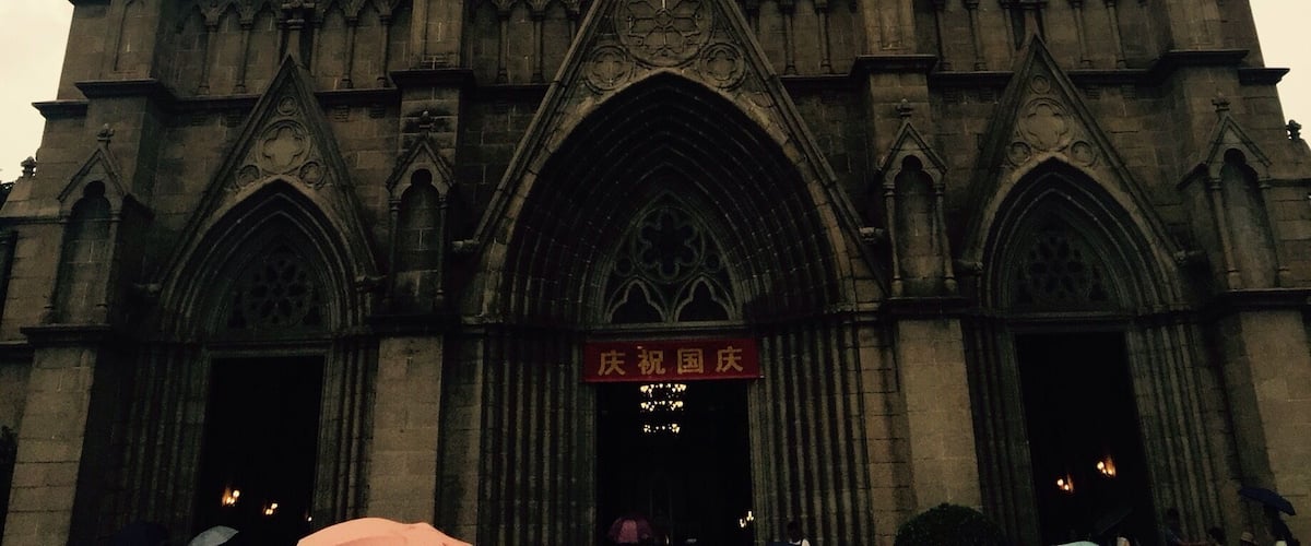 A Gothic cathedral with twin spires, a large rose window, and a cross at the top.