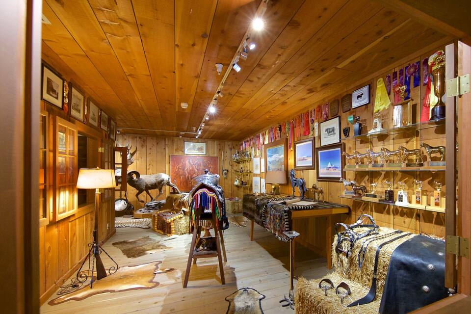 A rustic interior with wooden walls, a mounted ram sculpture, and various trophies and awards displayed on shelves.