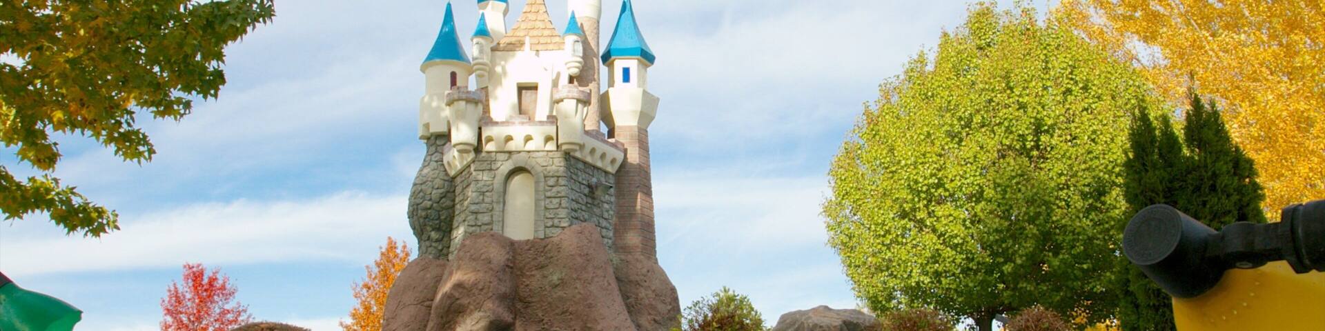 A castle with multiple towers and a flag on top, surrounded by trees and a paved area.