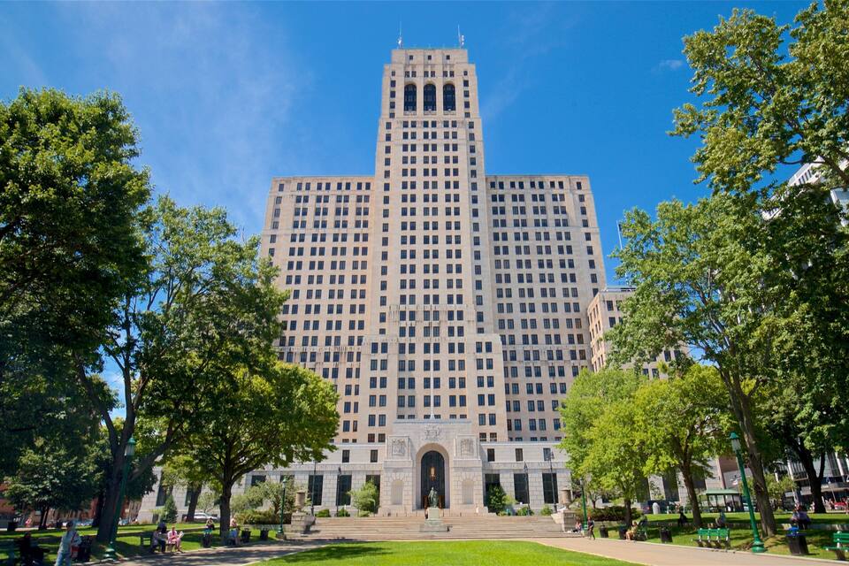 A large, historic building with a central tower and arched entrance, surrounded by a park with trees and benches.