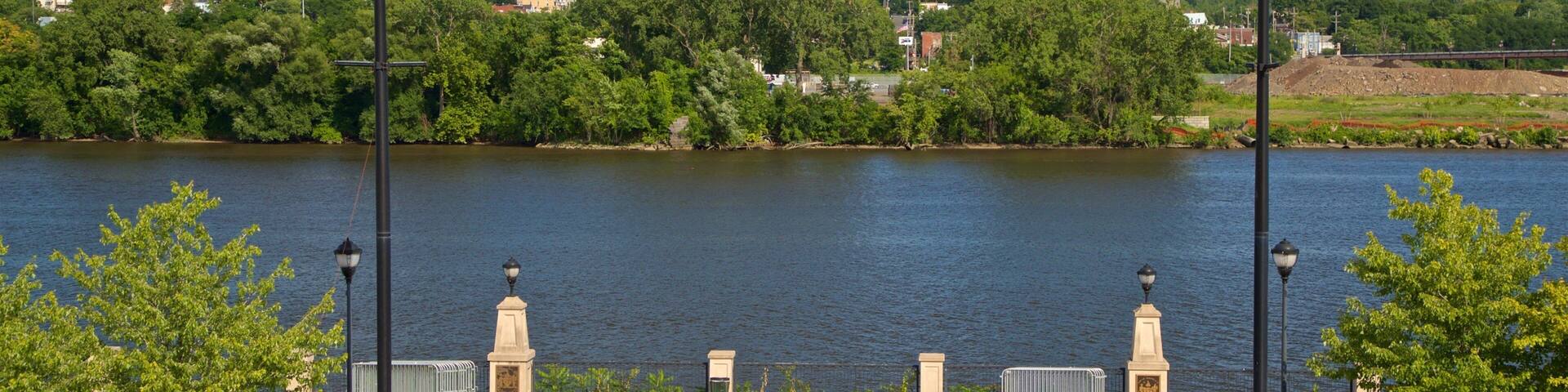 A riverside park with a paved walkway, lamp posts, and benches.
