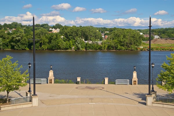 A riverside park with a paved walkway, lamp posts, and benches.