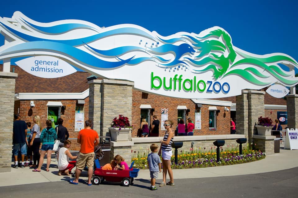 A Buffalo Zoo entrance with a large sign, a brick building, and people around.