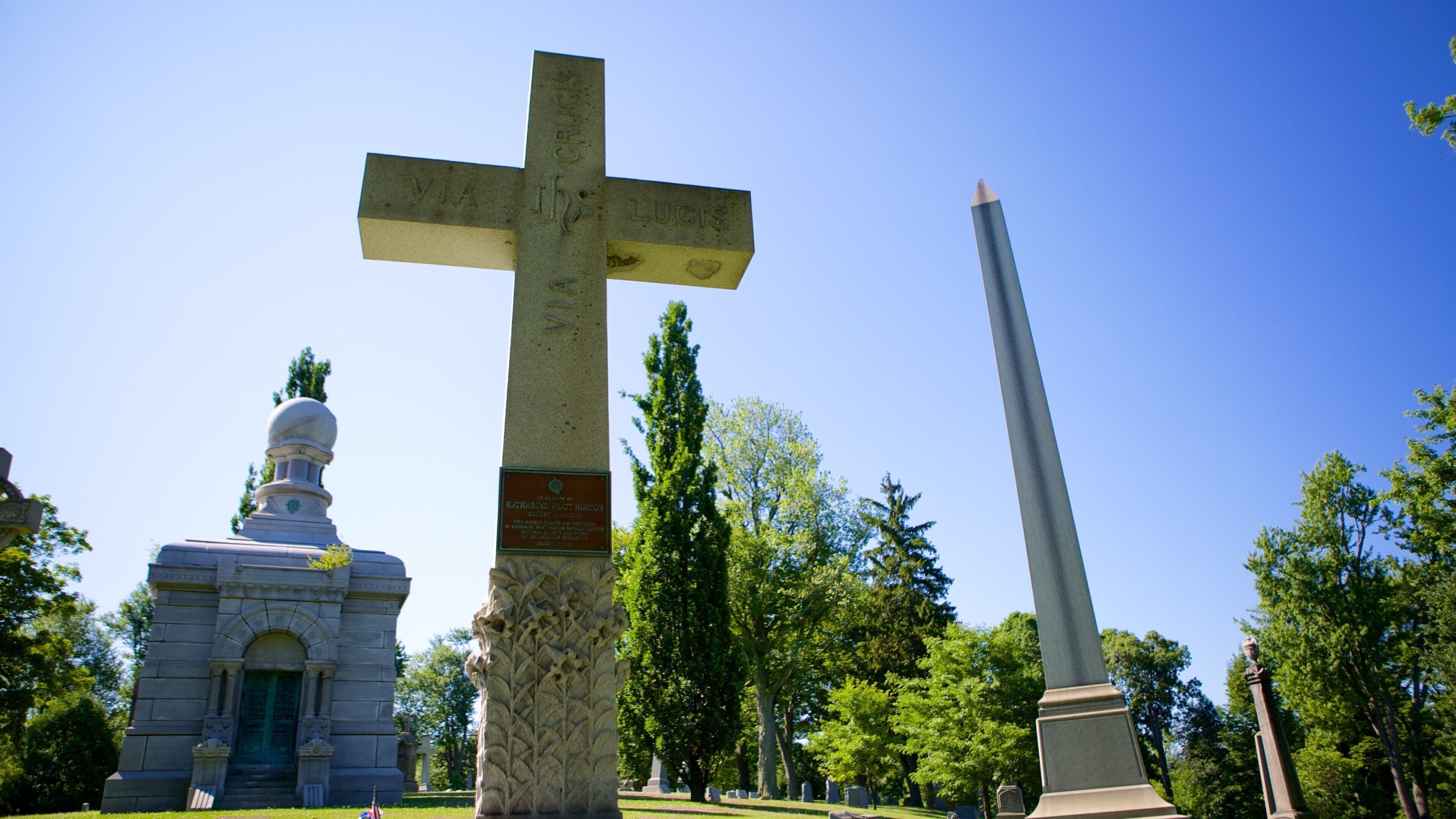 A cross, a tall obelisk, and a dome-shaped building in a park.