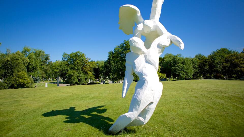 Eine weiße Skulptur einer Figur in einem Park, im Hintergrund grüne Wiesen und Bäume.