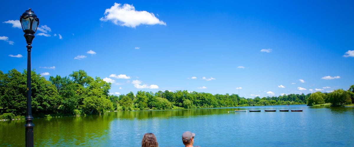 A couple sitting on a bench by a lake with boats, trees, and a clear sky.