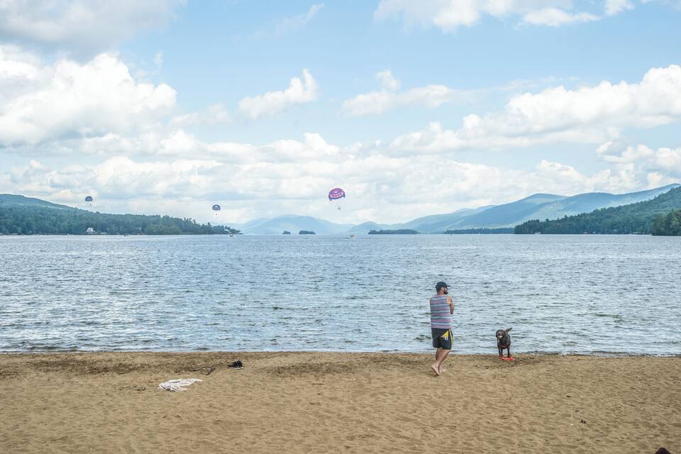 A beach with a person and a child watching kites over water.