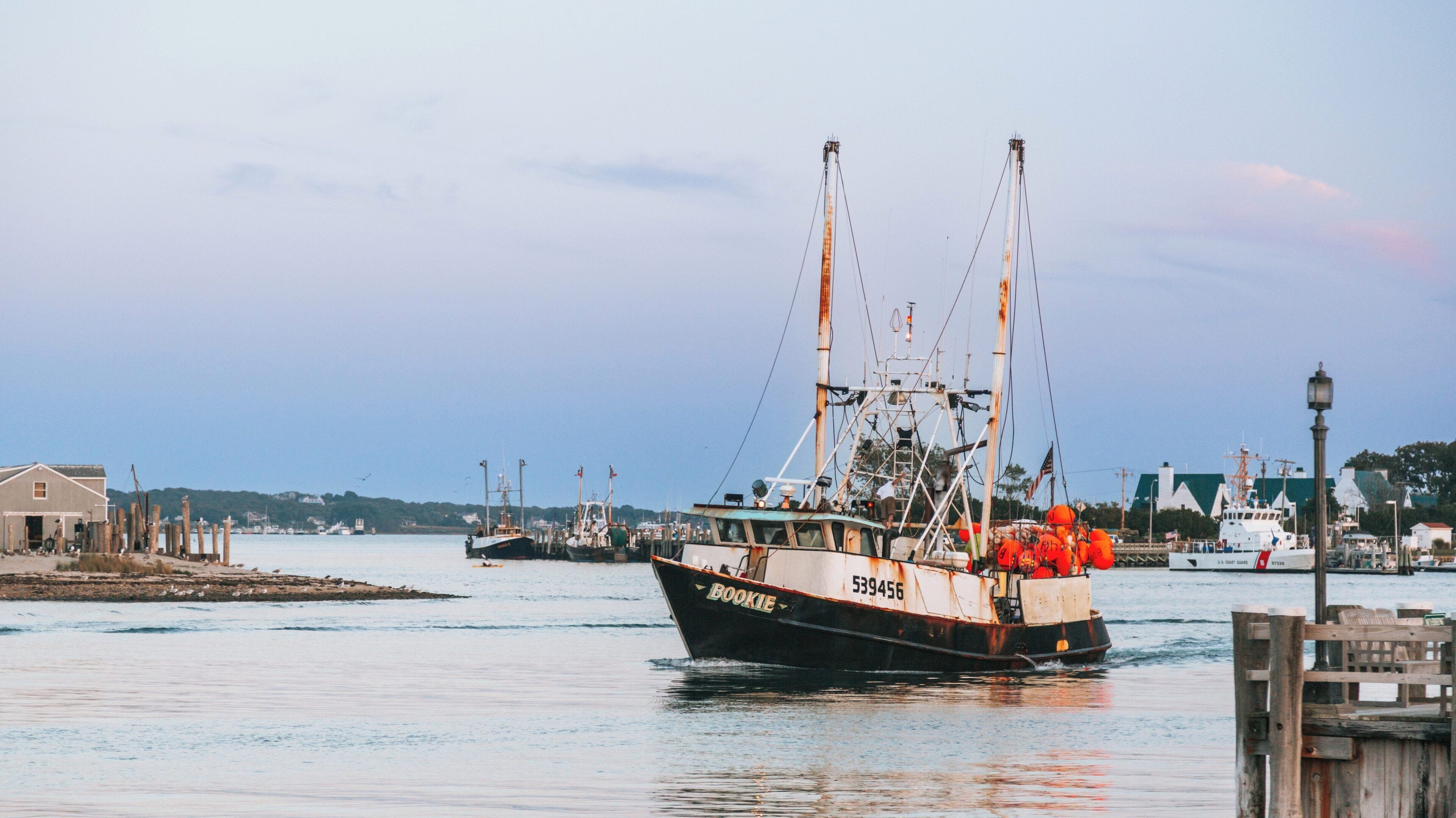 View of Montauk Point Lighthouse located in Montauk, New York with a fishing boat cruising along the calm waters at sunset, highlighting a beautiful coastal landscape