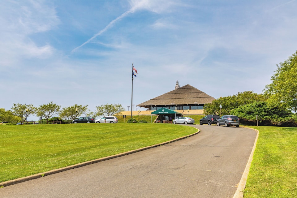 A curved road leading to a building with a green awning, a flagpole with an American flag, and a grassy area with trees.