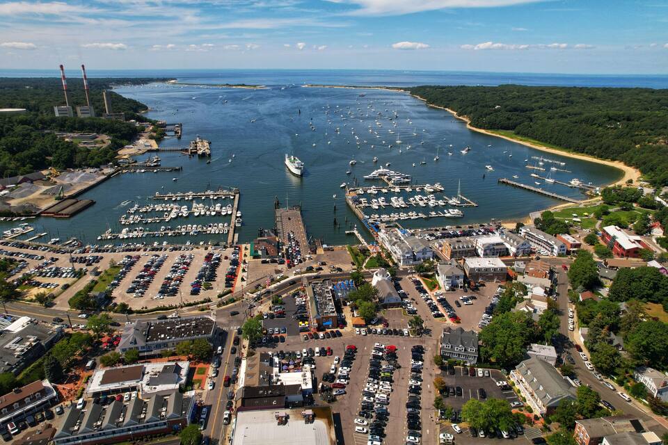 Un port de plaisance situé sur la côte, avec de nombreux bateaux, un grand navire et des bâtiments industriels environnants.