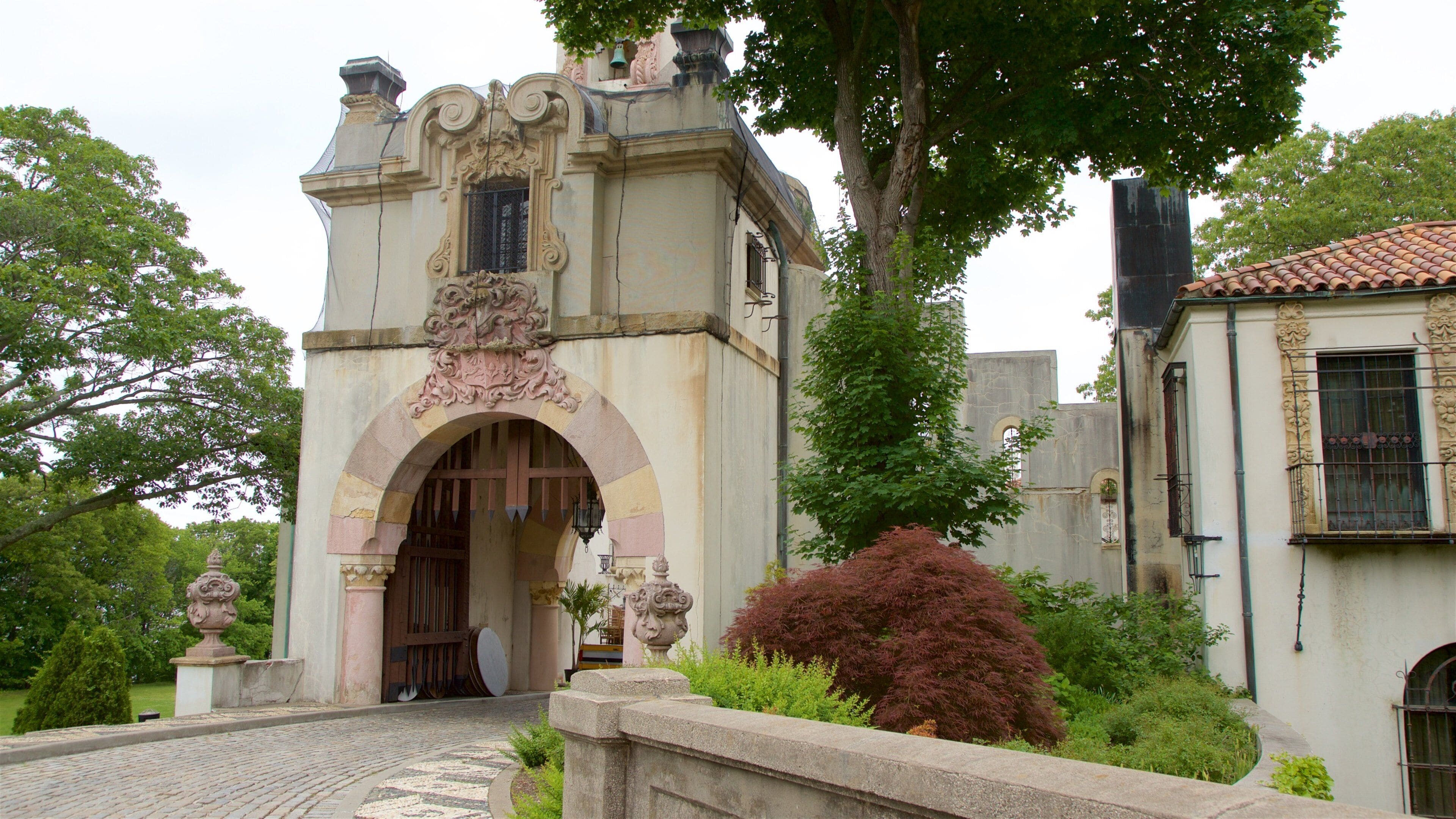 A historic building with an ornate entrance, a tiled roof, and lush greenery.