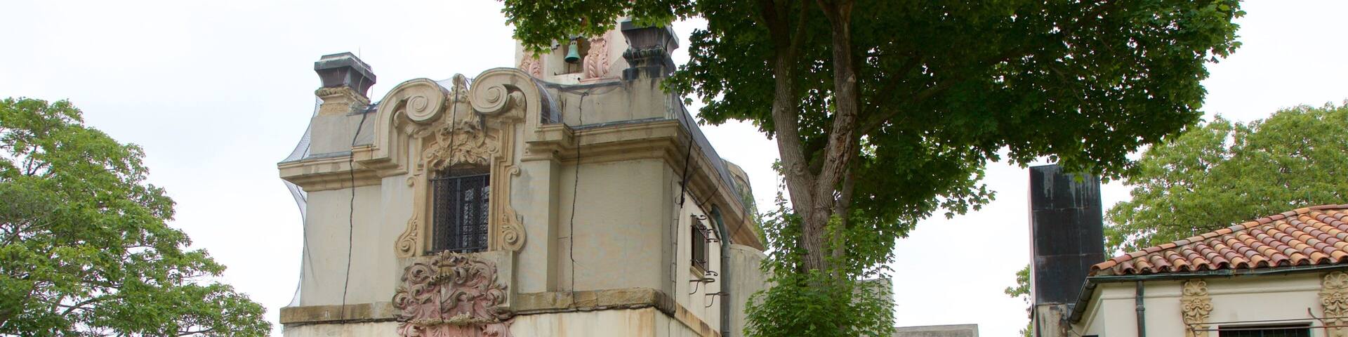 A historic building with an ornate entrance, a tiled roof, and lush greenery.