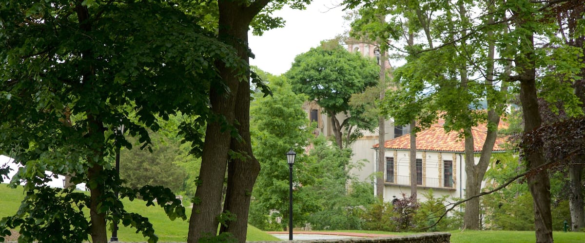 A stone wall, trees, and a building with a red-tiled roof.