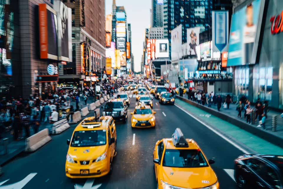 Una concurrida calle urbana con taxis amarillos, peatones y altos edificios con letreros iluminados.