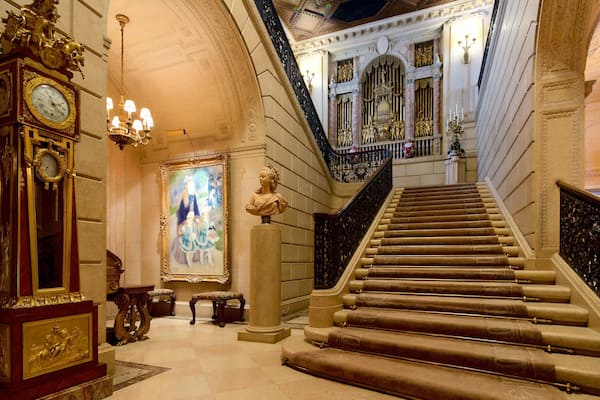 Uma escadaria imponente com grades ricamente decoradas, um relógio grande e um quadro emoldurado.