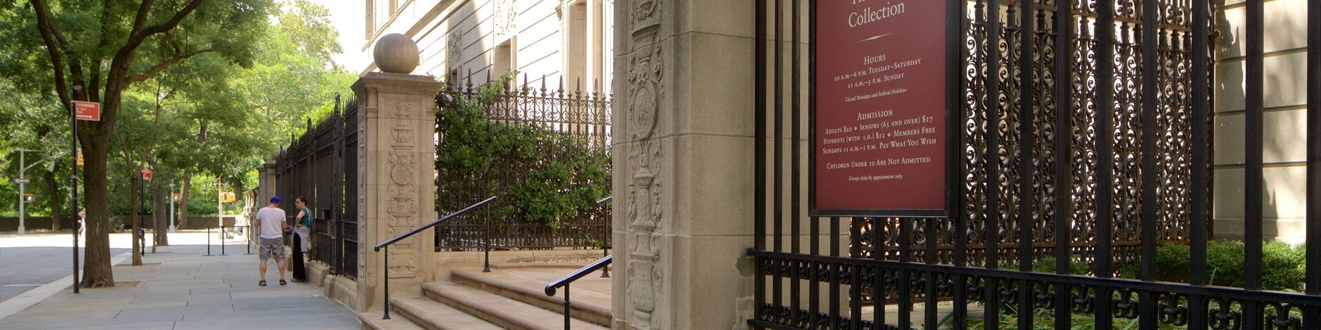A historic building with a wrought iron fence and a plaque detailing The Frick Collection hours and admission fees.