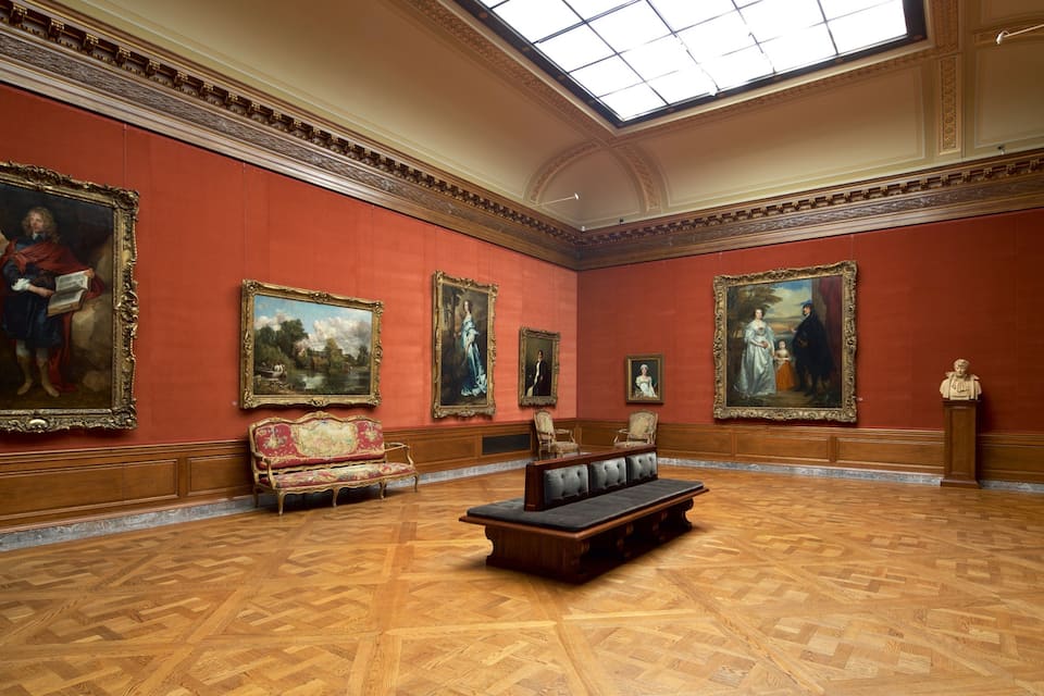 A grand art gallery with large paintings, ornate furniture, and a high ceiling.