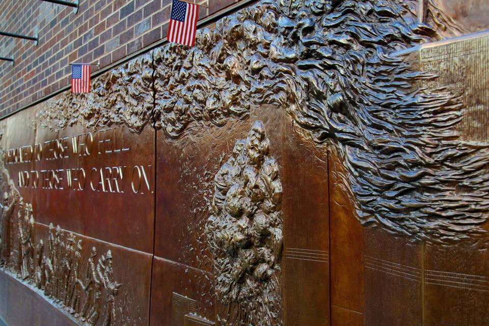 A bronze wall with relief sculptures and inscriptions, including American flags.