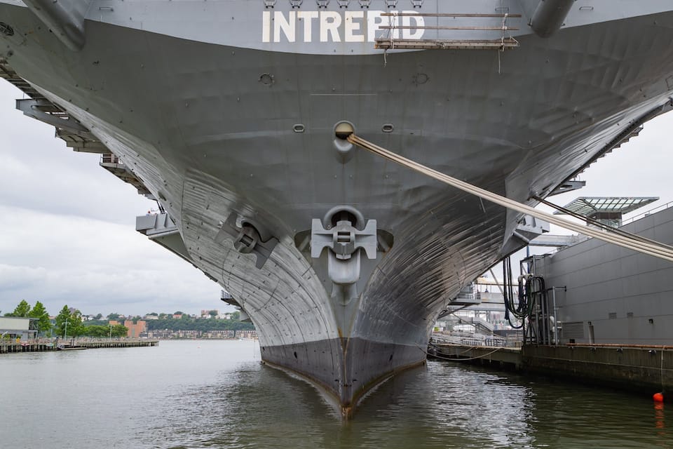 A large ship docked at a port with the name "INTREPID" visible on its bow.