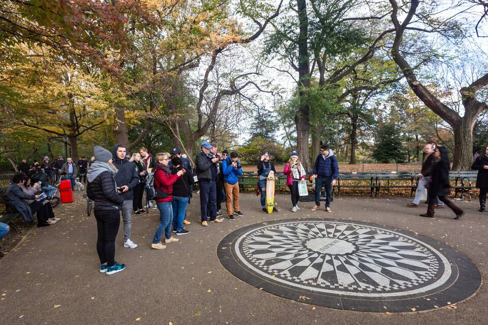 Un grupo de personas reunido alrededor de un diseño circular en un parque con árboles y bancos.