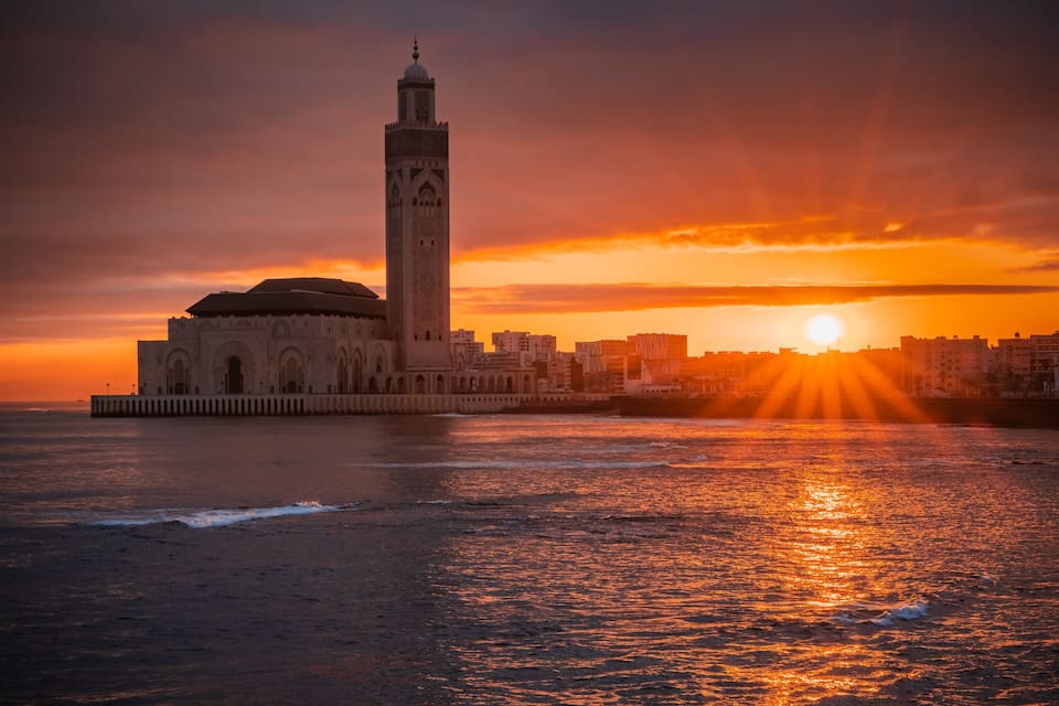 Una mezquita con un minarete alto junto al mar al atardecer.