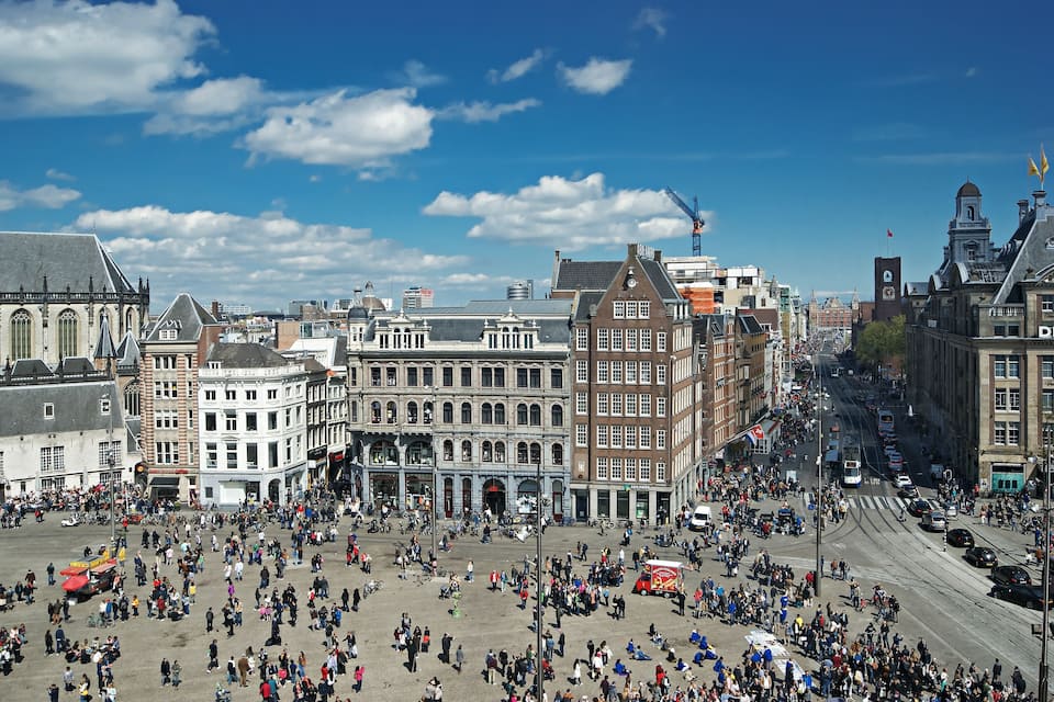 A bustling square with historic buildings, a tram, and a crowd of people.