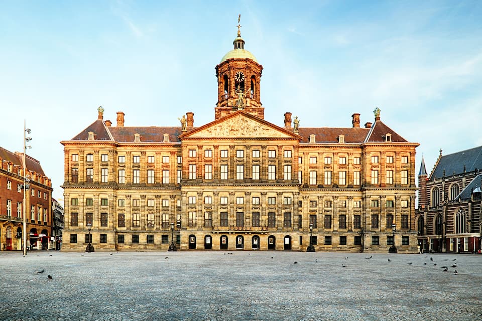 A large historic building with a prominent clock tower and a spacious courtyard.