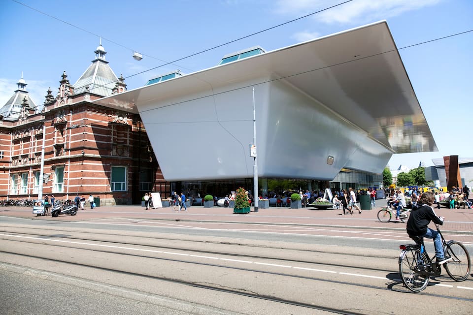 A modern building with a large white facade and a historic brick building in the background.