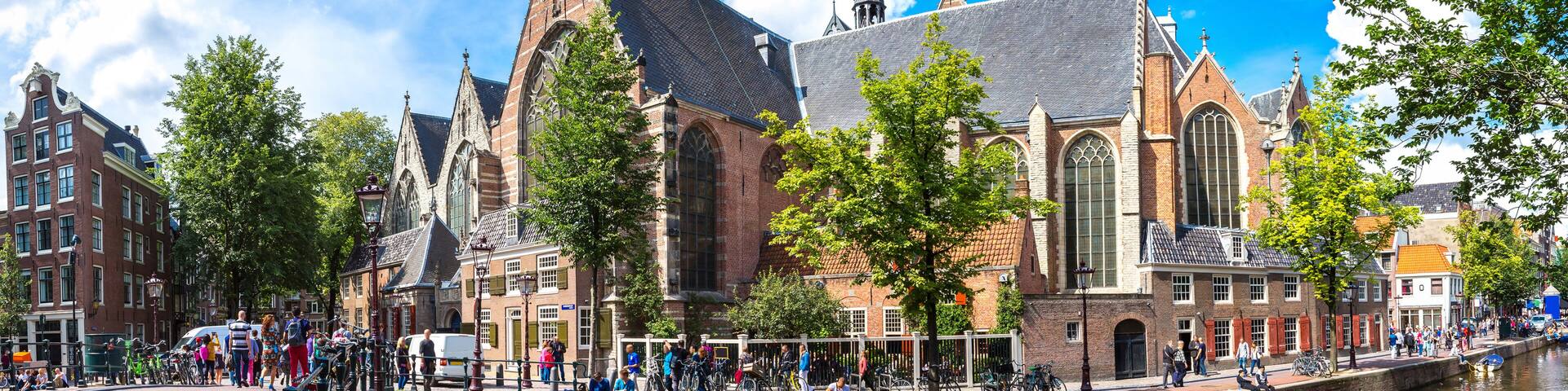 A historic church with a tall spire, a canal, and a bridge with people and bicycles.