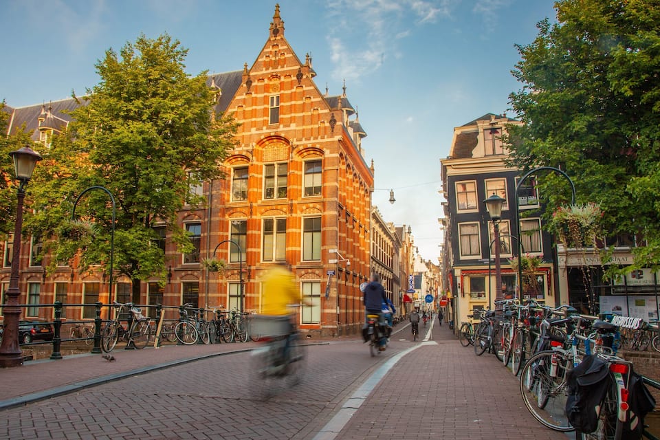 A cobblestone street lined with historic buildings, bicycles, and a cyclist.