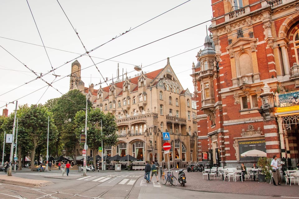 A street with tram tracks, historic buildings, and outdoor seating at a cafe.