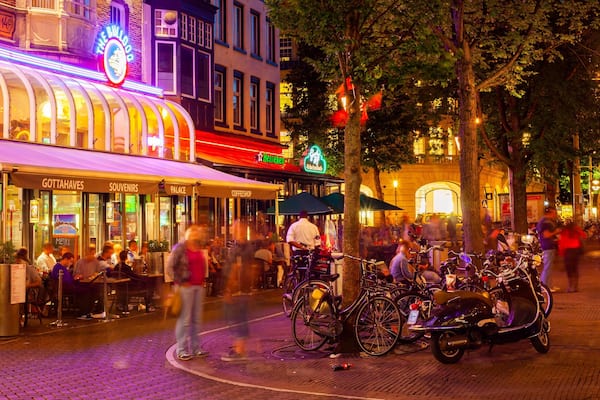 Eine belebte Straßenszene mit verschiedenen Geschäften und Cafés, darunter ein Heineken-Schild und ein Café namens 'Palace'.