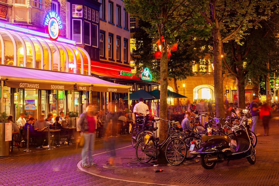 A lively street scene with a variety of shops and cafes, including a Heineken sign and a cafe named 'Palace'.