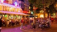 Une rue animée, avec une variété de boutiques et de cafés, dont une enseigne Heineken et un café appelé « Palace ».