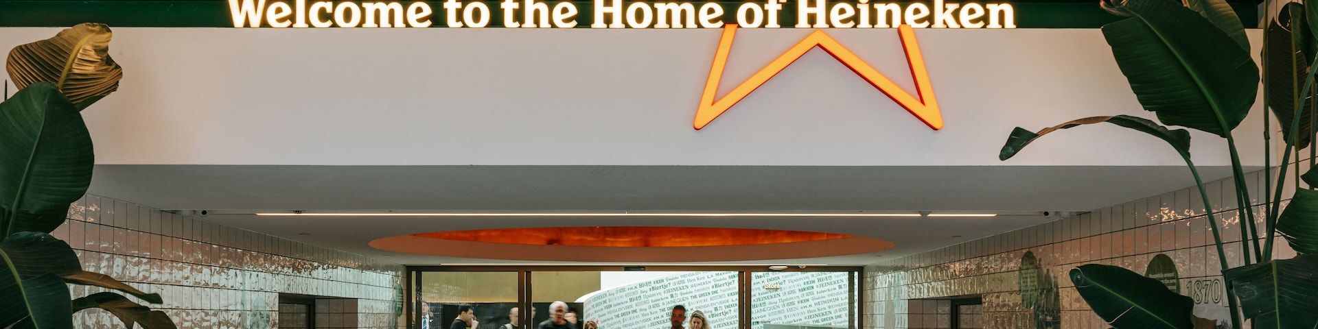 Ein modernes Interieur mit einem großen, beleuchteten Heineken-Logo und einem Schild mit der Aufschrift 'Welcome to the Home of Heineken'.