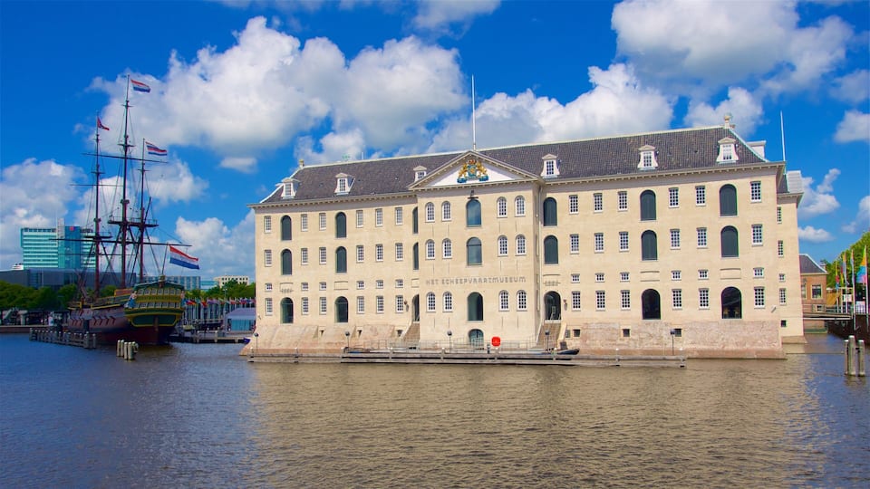 A historic building with multiple windows and a flag on top, situated by a body of water.