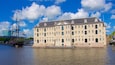 Een historisch gebouw met meerdere ramen en een vlag, gelegen aan het water.