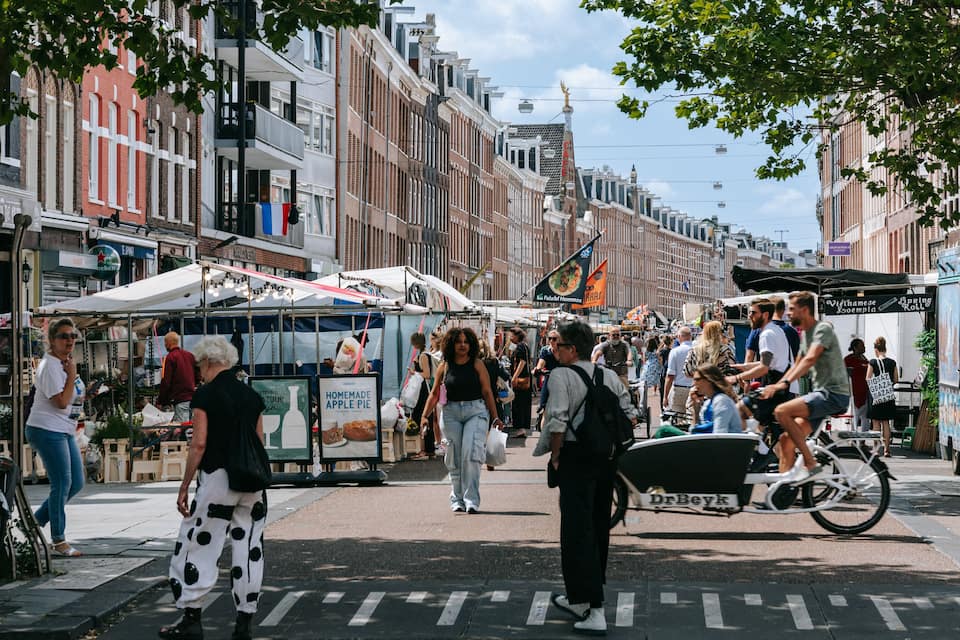 A busy street with people walking, a market stall, and a bicycle.