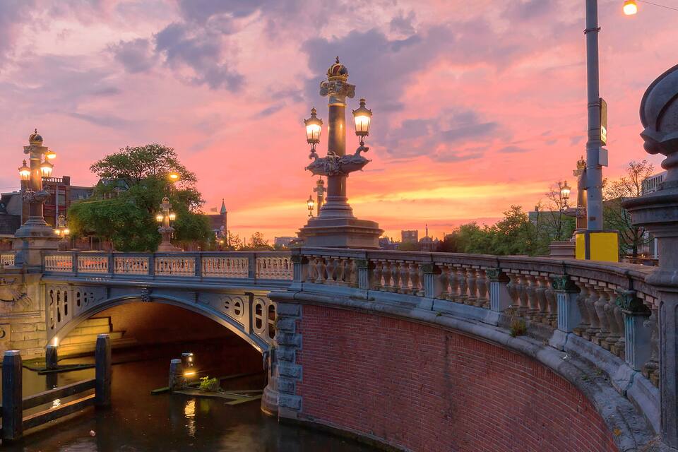 A bridge with ornate lamp posts and a statue, a canal beneath, and a sunset sky.