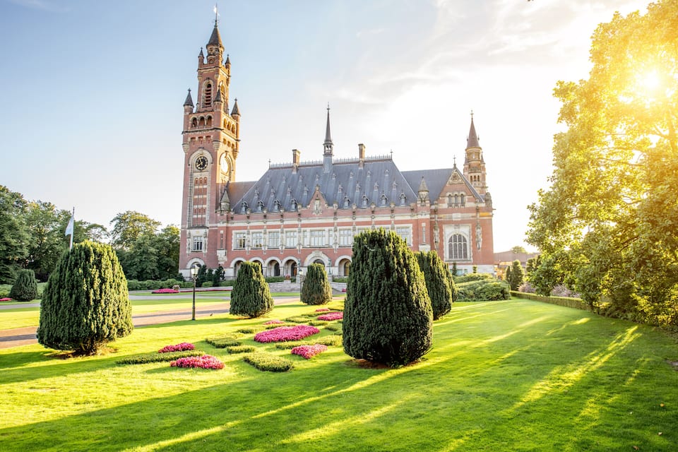 Een historisch gebouw met een klokkentoren, omgeven door goed onderhouden tuinen en bomen.