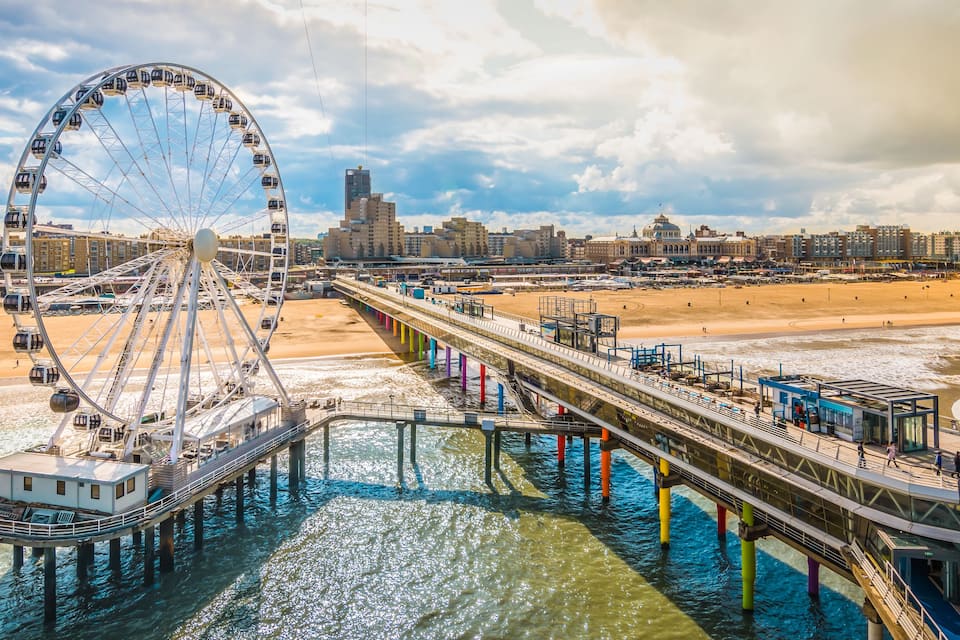 Uma roda gigante, um píer e uma paisagem urbana com edifícios e uma praia.