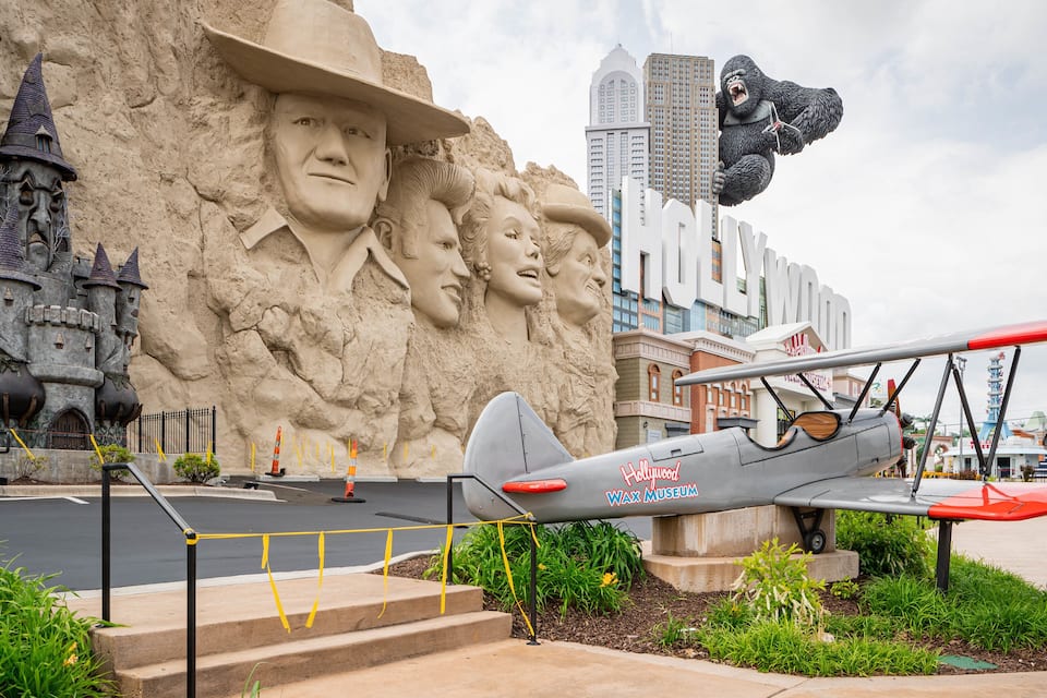 A large sand sculpture of a man with a hat, a vintage biplane, and the Hollywood sign.