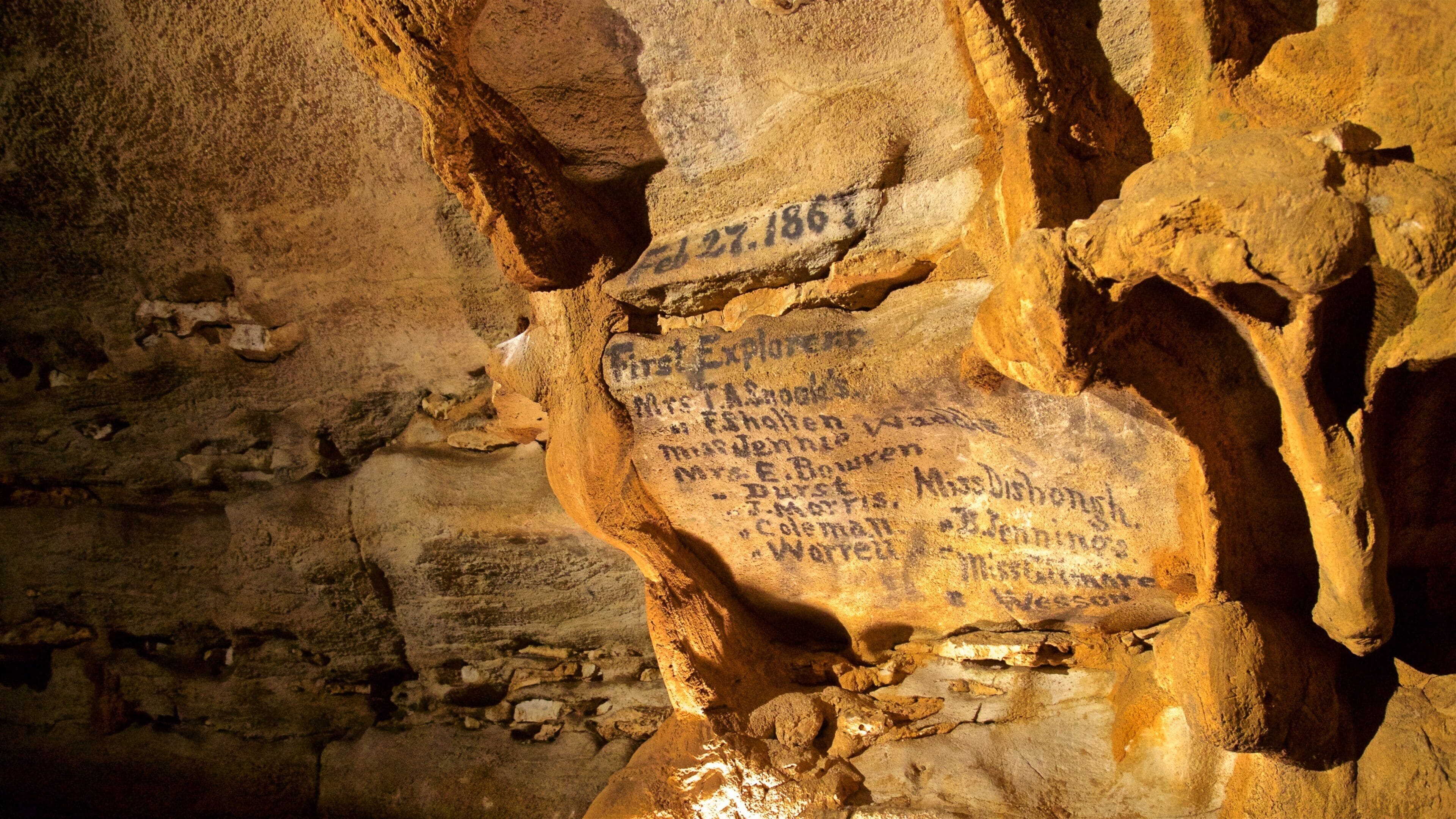 Un mur de grotte orné de noms et de dates gravés, notamment « 27 février 1863 » et « Premiers explorateurs ».