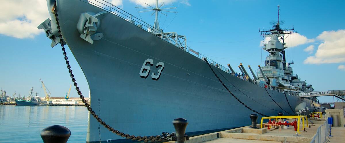A large naval ship docked at a port with a clear sky.