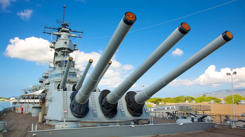A naval ship with multiple large guns, a control tower, and a clear blue sky.